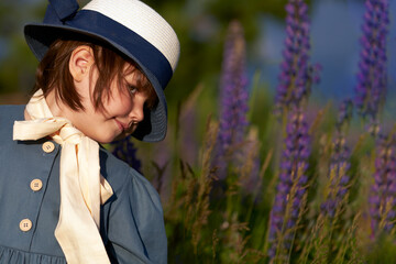 Portrait of a little girl in a retro style hat in a meadow with blue lupines .