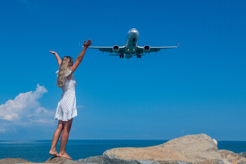 Aerial Rendezvous: Girl in White Dress on Stones, Plane Above the Blue Sea