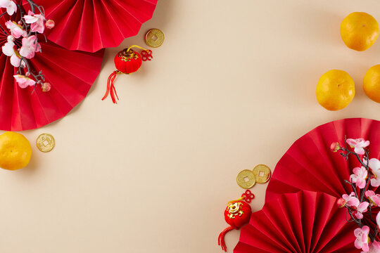 Embrace the grandeur of Chinese New Year. Top view flat lay of red paper fans, tangerines, gold coins, decorative essentials, sakura bloom on beige background with advert panel