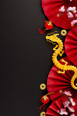 Cheers to Chinese New Year 2024. Top view vertical photo of gold dragon, red featuring fans, auspicious coins, decorative elements, sakura on black background with promo area - obrazy, fototapety, plakaty