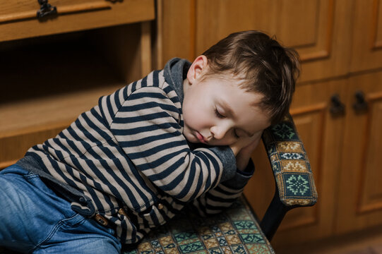 Little handsome boy, child sleeps, lying on an armchair in the room. Photography, portrait, lifestyle.