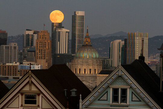 November, a full moon is rising over San Francisco's Painted Ladies and City Hall. 