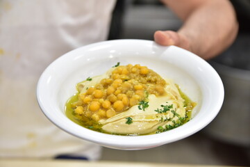 Bowl with hummus dip with chickpea in hand with olive oil and parsley