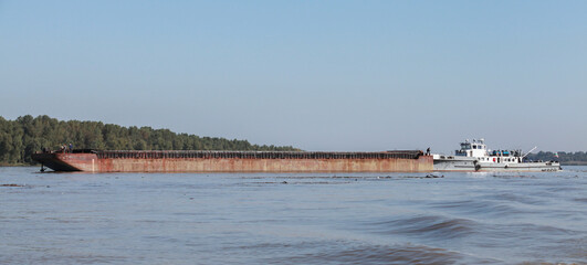 A pusher boat transports cargo barge along a river