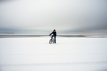 Teenager rides a bicycle in winter in a snowy area