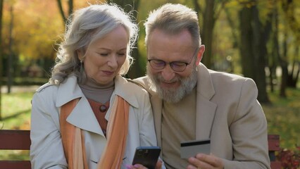 Happy Caucasian married couple mature old man woman grandparents using smartphone credit card bank app shopping online senior family make order purchase mobile phone easy buying in autumn park city - Powered by Adobe