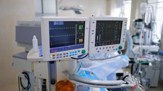 Monitors of lung ventilator machine displaying the life signs of a patient. Top vie won the modern surgery with a variety of equipment and surgeon working at backdrop.