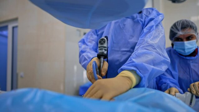 Gloved hands of unrecognized surgeon apply endoscopic device. Assisting nurse holds the ultrasound transducer.