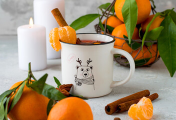 White cup with mulled wine, spices, cinnamon, tangerines on branches with leaves, apple and...