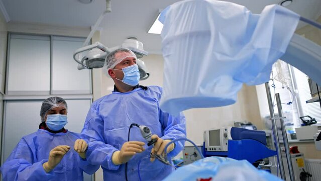 Female nurse assisting male surgeon at endoscopic operation. Professional doctor looking intently on the monitor.