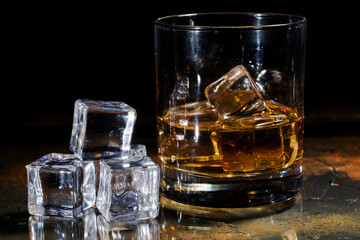 Glass of whiskey and ice cubes in the foreground. Space for text.