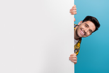 Photo of young funny happy guy hiding white wall billboard information banner with promo details...