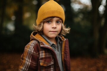 A portrait of a cute little boy in a yellow hat and coat in the autumn forest.