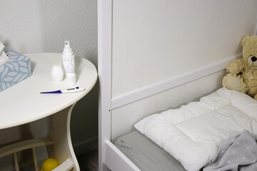 Flue medicine bottles and a thermometer on white table near bed with teddy bear in baby room