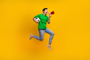 Full length photo of energetic man jumping hold soccer ball scream in loudspeaker at empty space...