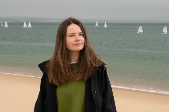 Portrait of a young woman on the beach with windsurfers in the background