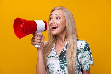 Photo of overjoyed girl with long hairdo dressed print shirt scream in loudspeaker look empty space isolated on yellow color background