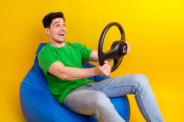 Full length photo of funny man dressed green t-shirt sit on pouf hold steering wheel look empty...