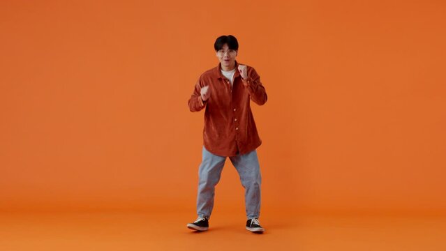 Cheerful asian man silly dancing over orange background