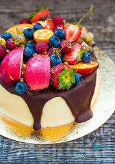 Delicious cheesecake with melted chocolate, apples, strawberries, blueberries, peaches, raspberries and kumquats on the top, rustic background