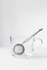 Silver mesh tea strainer in  a glass cup, glass mug with tea leaves infuser on white background