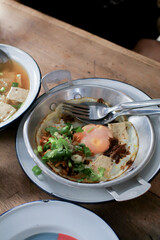 Fried eggs in a small pan with ham, minced pork on wooden table, Thai Breakfast called Kai Kata. Vietnam food.
