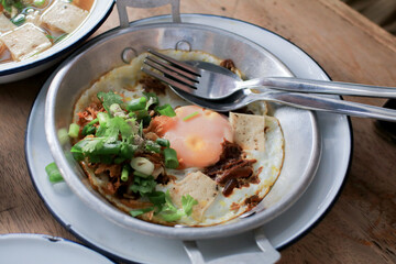 Fried eggs in a small pan with ham, minced pork on wooden table, Thai Breakfast called Kai Kata. Vietnam food.
