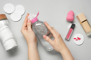 Woman using makeup remover, closeup. Cotton pads, lip gloss, foundation and sponge on light grey background, top view - obrazy, fototapety, plakaty