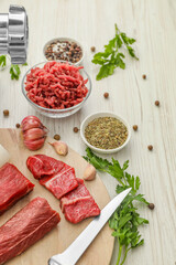 Meat grinder, beef, garlic, parsley and spices on white wooden table