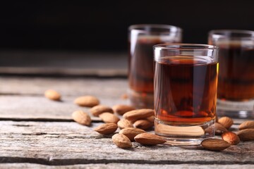 Shot glasses with tasty amaretto liqueur and almonds on wooden table, closeup. Space for text