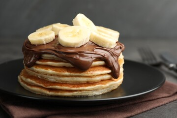 Tasty pancakes with chocolate spread and sliced banana on table, closeup