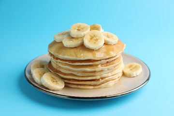 Tasty pancakes with sliced banana and honey on light blue background