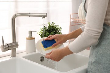 Woman washing plate at sink in kitchen, closeup