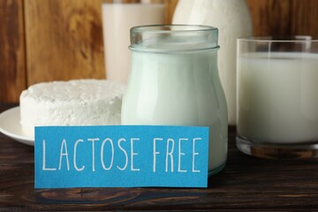 Card with phrase Lactose free and different fresh products on wooden table, closeup