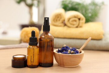 Bottles of essential oils, dry flowers and jar with cream on light wooden table. Spa therapy