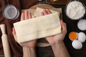 Man holding raw puff pastry dough at wooden table, top view