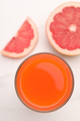 Tasty grapefruit juice in glass and slices of fresh fruit on white table, top view