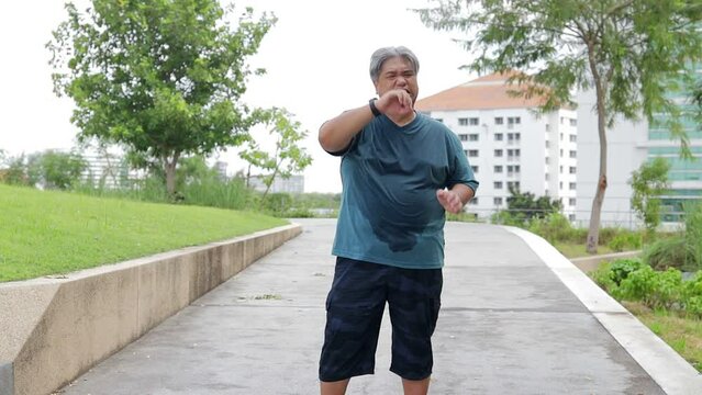 Fat Asian man jogging outdoors in the park. He felt very tired and had heatstroke. Sports concept, weight loss.