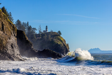 King tides at Cape Disappointment stae part. Large waves crashing on a cliff with a lighthouse in a background