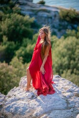 Woman sunset sea red dress, back view a happy beautiful sensual woman in a red long dress posing on a rock high above the sea on sunset.