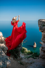 Red dress sea woman. Happy woman with flowing hair in a long flowing red dress stands on a rock...