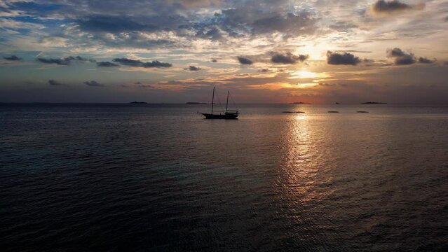 Aerial view of a masted sailing ship at sunset moored in Dhangethi Lagoon, Maldives, Indian Ocean
