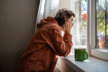 Introverted teenager spending time alone at home in warm sunny day, looking at window...