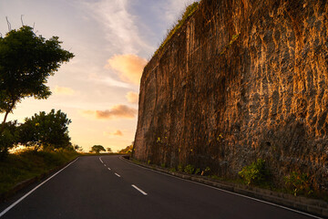 The cliff overhangs along the road to the ocean at sunset.