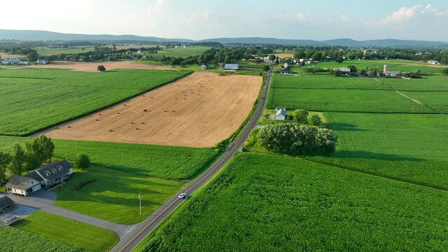 Rural USA during summer. Aerial view of cars driving on country road surrounded by farms and green fields.
