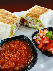 tantalizing display of a meal. The centerpiece is a burrito, cut in half to reveal a filling of meat and lettuce, among other ingredients. The burrito’s exterior is toasted to a golden brown, adding t