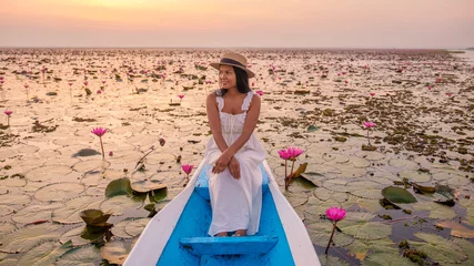 Foto op Plexiglas The sea of red lotus, Lake Nong Harn, Udon Thani, Thailand. Asian woman with a hat and dress on a boat at the Red Lotus Lake in the Isaan © Fokke Baarssen