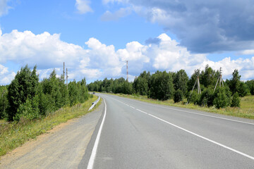 Fototapeta premium Empty highway surrounded by forest. Beautiful summer landscape, white clouds on a blue sky.