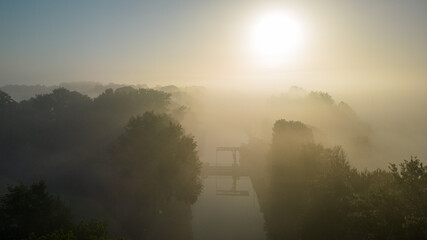 This evocative image captures the delicate balance of light and mist at dawn, with the sun rising...