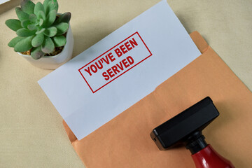 Red Handle Rubber Stamper and You've been served text above Brown envelope isolated on wooden...